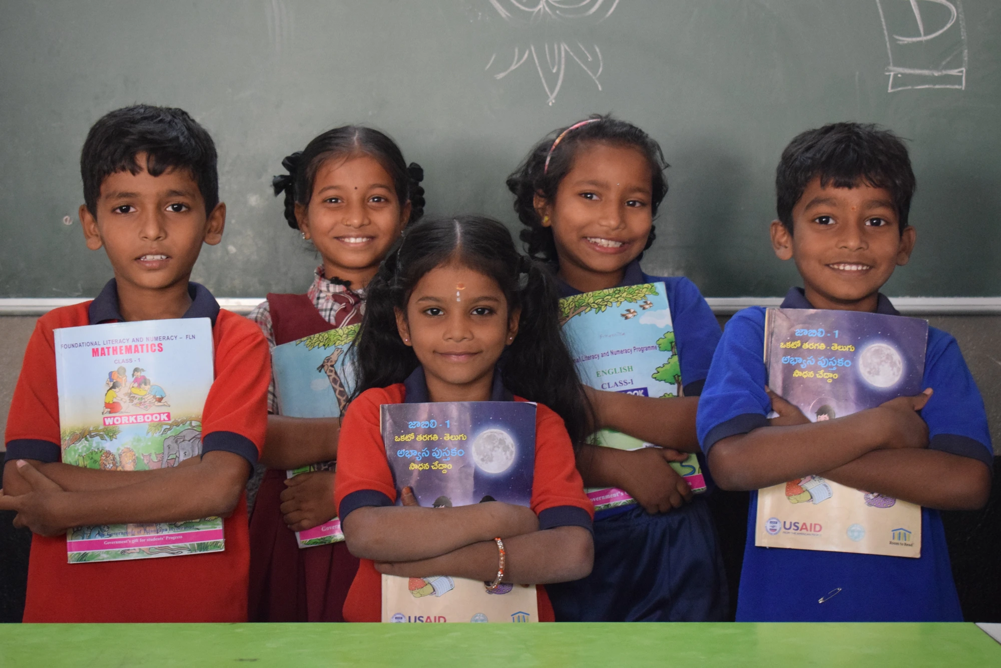 Students holding their new workbooks in front of the classroom blackboard